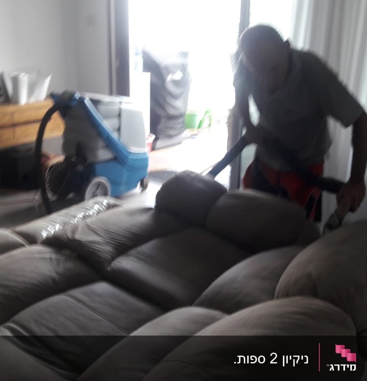 אדם מנקה ספה עם שואב אבק מקצועי